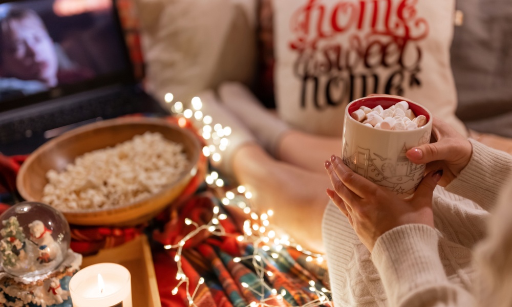 Moscow 11.29.2021. woman drinking cocoa cup with marshmallow in hand holding and watching the movie home alone on laptop at home in cozy bed and popcorn food at night on christmas or new year eve