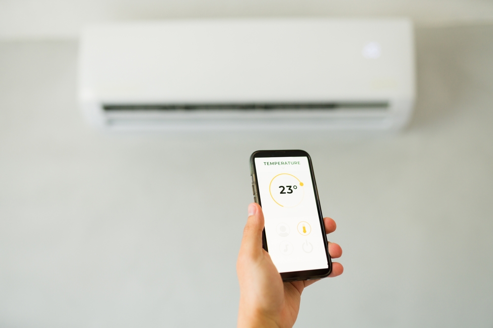 Closeup of a man holding a smartphone and controlling the temperature of an air conditioner with a mobile app in a bedroom