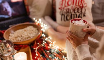Moscow 11.29.2021. woman drinking cocoa cup with marshmallow in hand holding and watching the movie home alone on laptop at home in cozy bed and popcorn food at night on christmas or new year eve