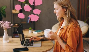 Α woman sitting nexto to her laptop and mobile phone, drinking a cup of coffee