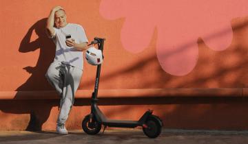 A guy standing next to a Xiaomi electric scooter, smiling and looking at his phone